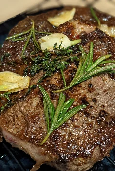 Close-up shot of a thick grilled ribeye steak topped with fresh rosemary sprigs and butter.