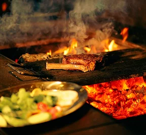 Selection of grilled meats and colorful sautéed vegetables cooking over hot coals on a live grill.