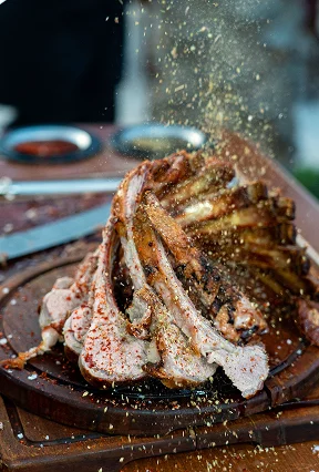 Gourmet roasted rack of lamb sprinkled with herbs and spices served on a round wooden cutting board.